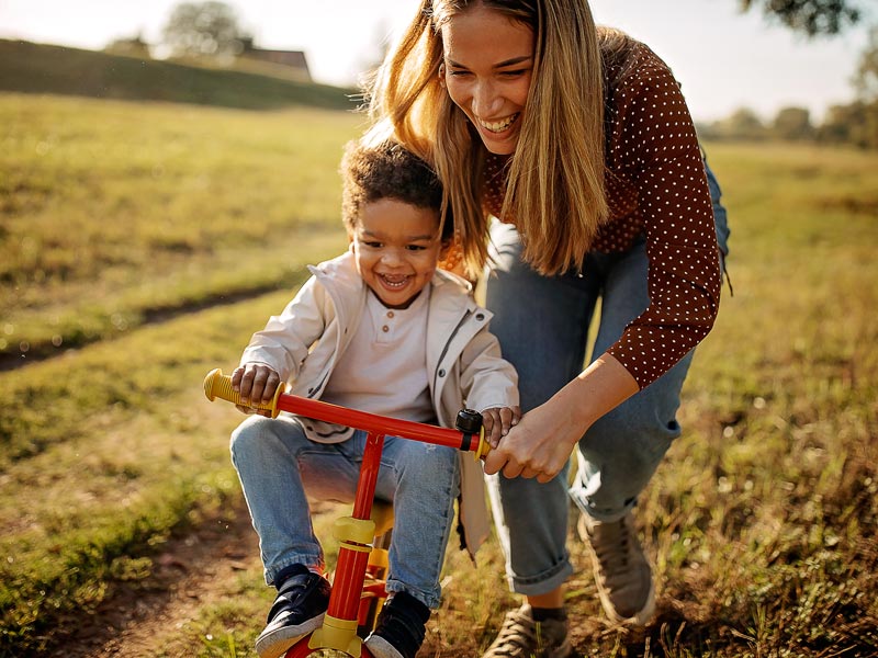 young woman teaching little boy to ride tricycle
